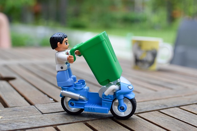 Figurine qui transporte une poubelle verte sur un deux roues